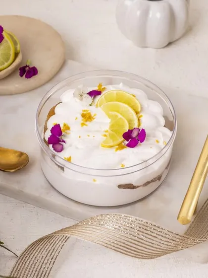 A zesty key lime pie dessert tub. The garnish of fresh lime slices and edible flowers immediately communicates the flavour and freshness of the dessert.