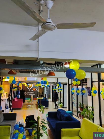 Decorating a large office lounge area with blue and yellow balloon clusters for a corporate event.