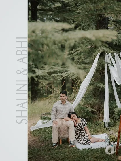 A quiet, romantic moment during a picnic-themed pre-wedding shoot. The setup with the flowing white drapes adds a touch of softness to the rustic forest setting.
