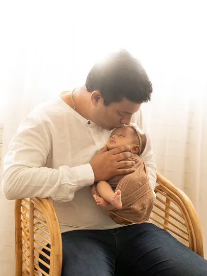 A father's gentle kiss for his sleeping newborn. The warm sunlight and natural setting create a peaceful and loving atmosphere.