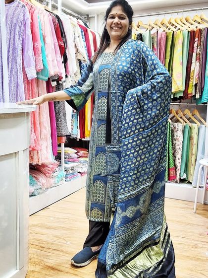Standing in my boutique, surrounded by racks of colorful kurtis and fabrics. I am wearing a comfortable and stylish kurti made from our soft modal Ajrakh fabric.