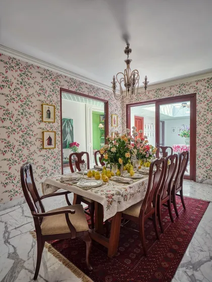 The dining room feels like a memory dressed up for the evening. Blush-toned floral wallpaper, refurbished furniture, and a mix of heritage prints create a space that is both elegant and warmly inviting.