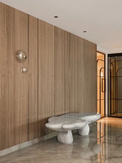 This entrance foyer is an exercise in warm minimalism. We used soft textures like the fluted wood wall paneling and a sculptural stone-like bench to create a calm, grounded feeling. The bubble-like wall lights add a touch of playful elegance.
