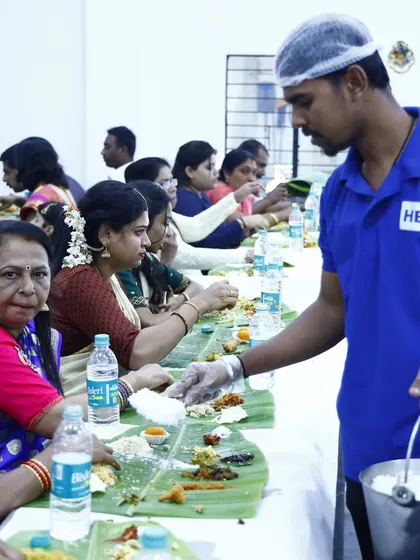 Our professional server, in full uniform with a hairnet and gloves, carefully serves rice to guests during a traditional banana leaf service, ensuring hygiene and attentiveness.