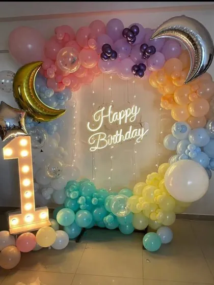 A dreamy 'Twinkle Twinkle Little Star' first birthday theme. This beautiful setup features a circular balloon arch in a rainbow of pastel colors, moon and star foil balloons, a light-up number '1', and a 'Happy Birthday' neon sign.