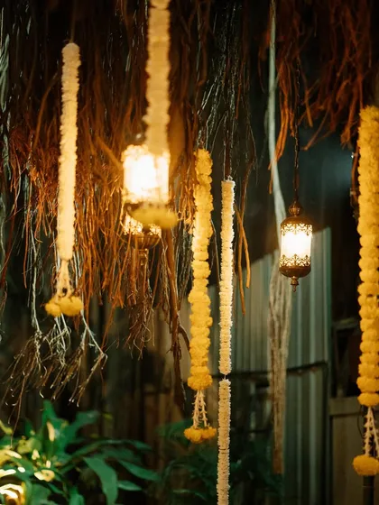This nighttime view highlights the magical ambiance created by combining floral garlands and vintage lanterns. The decor, set against the dark backdrop of foliage, is perfect for an evening wedding or festival.