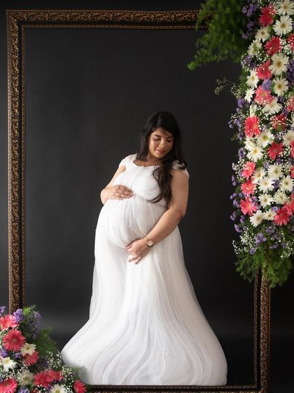 A gentle and serene pose within the floral frame. The combination of the dark background, fresh flowers, and the white gown is simply breathtaking.