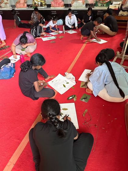 Campers are deeply focused on their nature painting projects, using leaves, flowers, and soil to create beautiful images.
