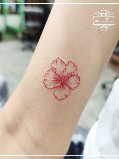 A single hibiscus flower outlined in red ink. This fine line floral tattoo is a great example of how a simple design with a single color can make a bold and beautiful statement.