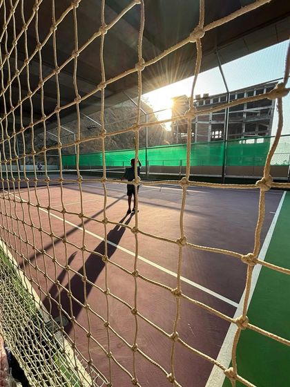 A view of the tennis court through the net as the sun sets. It's the perfect time for a focused, peaceful practice session.