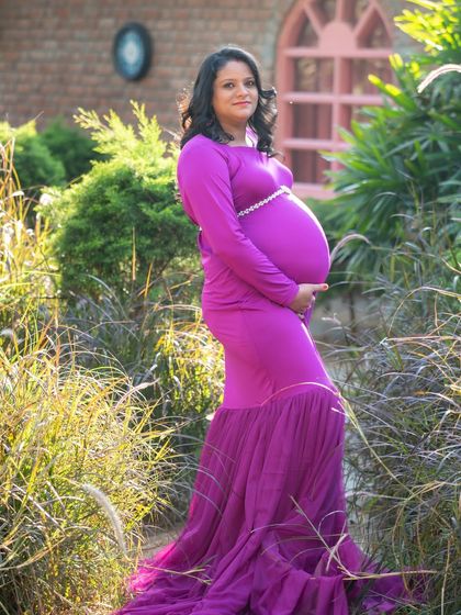 A beautiful profile shot of a mom-to-be in a vibrant purple gown, surrounded by lush greenery. The golden hour light adds a warm glow to this outdoor portrait.