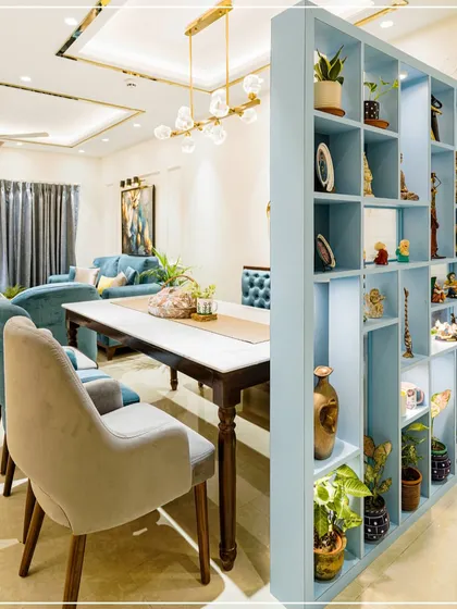 A dining area featuring a light blue shelving unit that acts as a partition, with a marble-top table and plush chairs.