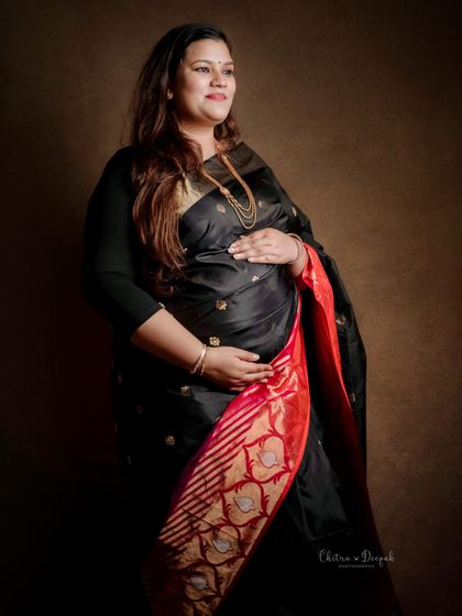 A classic and graceful pose in a black silk saree. The lighting is designed to highlight the rich fabric and the beautiful baby bump.