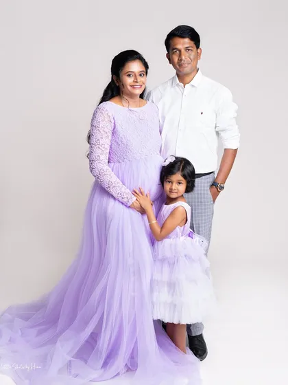 A full-length family portrait from a maternity session, showcasing the beautiful flowing lavender gown. The whole family stands together, creating a formal yet loving image.