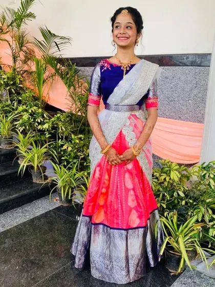 I designed this beautiful half-saree lehenga for a young woman. It features a pink pattu lehenga with a silver border, paired with a custom embroidered blue blouse and a silver dhavani.