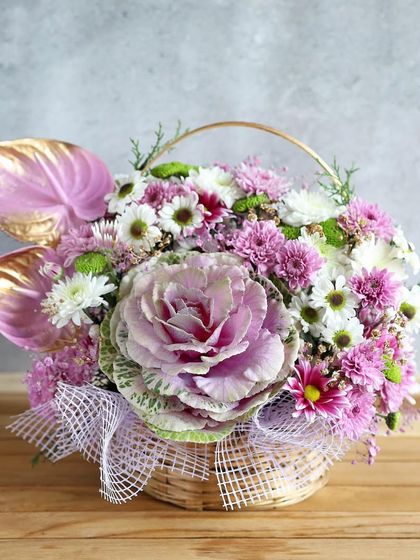 An elaborate and beautiful basket arrangement featuring a large ornamental cabbage flower, a truly unique and eye-catching gift.
