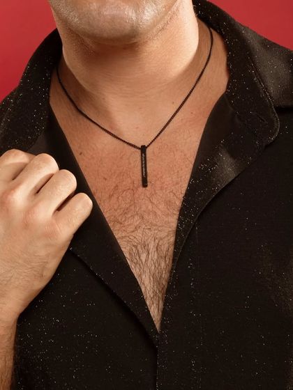 A close-up of a man wearing a black bar pendant on a cord necklace. This highlights a different style option from the standard metal chain, offering a more casual look.