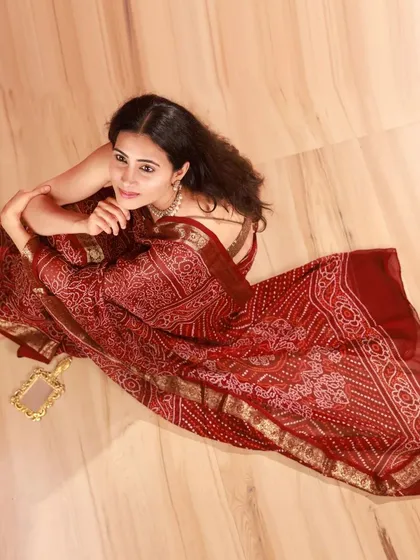 A top-down view of the model seated on the wooden floor. This angle allows the beautiful print of the saree to be fully appreciated.