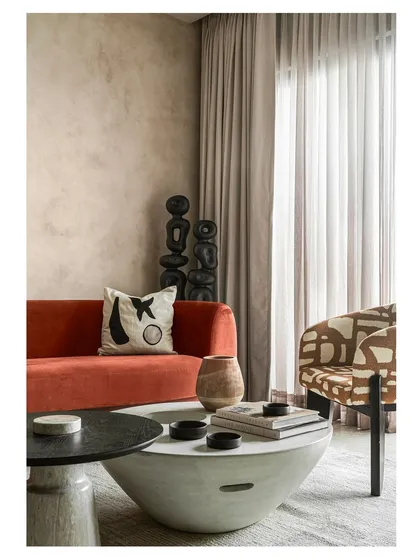 This shot captures the eclectic mix of furniture and decor in the living room. The patterned armchair, tribal-inspired sculptures, and mix of coffee table shapes come together to create a curated, textural experience.
