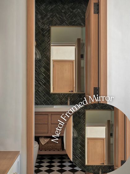 A metal-framed mirror adds a touch of industrial chic to this bathroom. The reflection shows the warm wooden door, creating a beautiful contrast with the dark herringbone tiles and checkerboard floor.