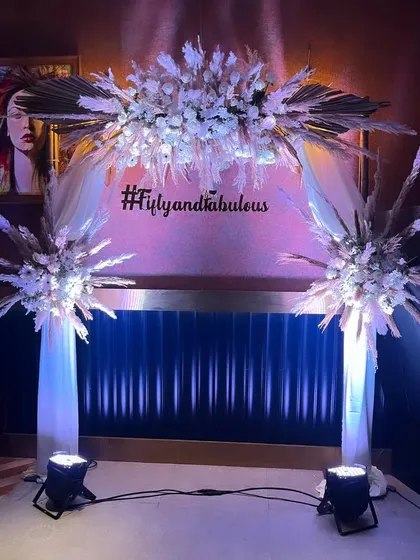 A stunning floral archway with white flowers and pampas grass. This "Fifty and Fabulous" setup is perfect for a milestone anniversary or birthday party.