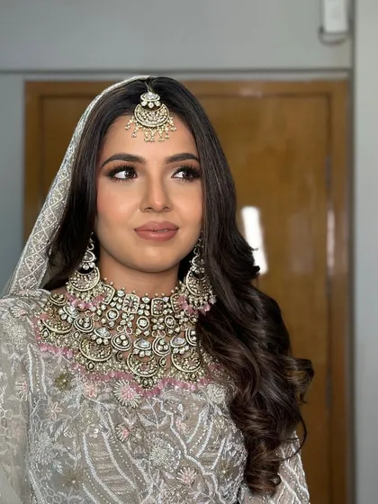 A side glance from the bride. Her hair is styled in deep, glamorous waves under a delicate dupatta, a perfect look for a daytime wedding ceremony.