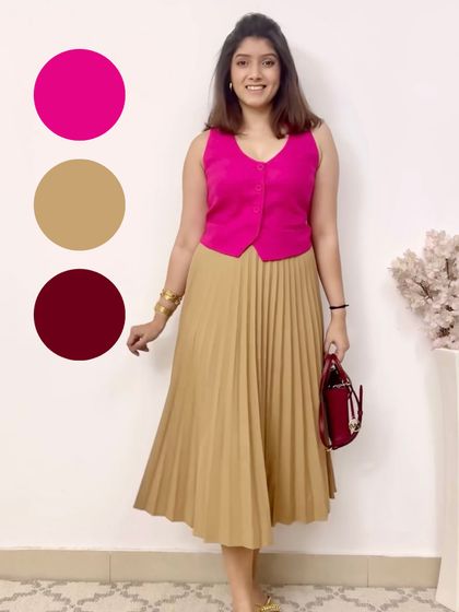 A bold and playful color combination. The bright pink waistcoat pops against the neutral beige pleated skirt, with the burgundy bag adding another layer of color.