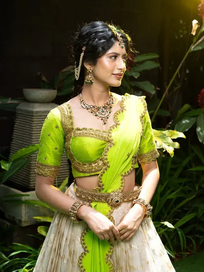 Wrapped in elegance, this half saree features a light gold tissue lehenga paired with a vibrant lime green princess katori blouse. The entire ensemble, including the dupatta, is finished with intricate handwork for a look of traditional grace.