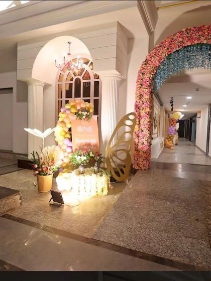 The entrance area of the venue, featuring a welcome corner, a decorated baby entry cart, and a floral archway leading into the main hall.