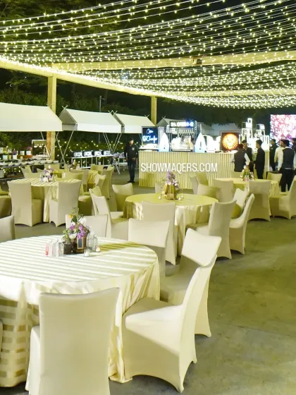 An overview of an outdoor reception area. The space is defined by a ceiling of warm string lights, with a mix of round tables and lounge seating to encourage guest interaction.