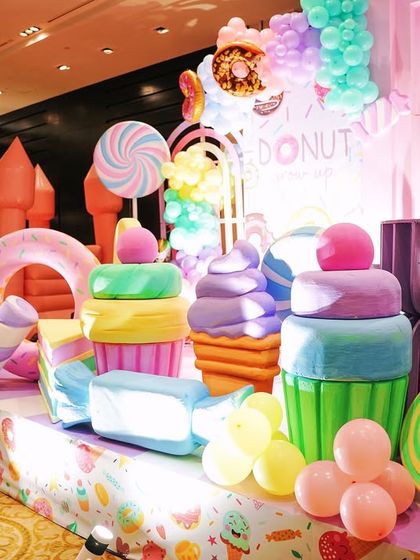 A full view of the Candyland stage area, showcasing a variety of large, custom made props including cupcakes, ice cream cones, and candy swirls. A pink bouncy castle is visible in the background, integrated into the decor.