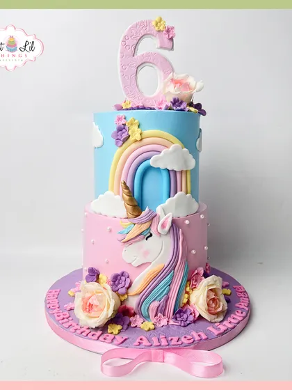 A magical two-tiered unicorn cake for a 6th birthday. This pastel creation features a beautiful unicorn, a rainbow, fluffy clouds, and delicate flowers, making it a truly whimsical and dreamy centerpiece.