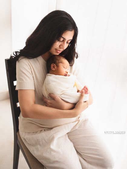 A mother gazes lovingly at her newborn, held close in her arms. This simple, light-filled portrait is delicate, warm, and full of emotion.