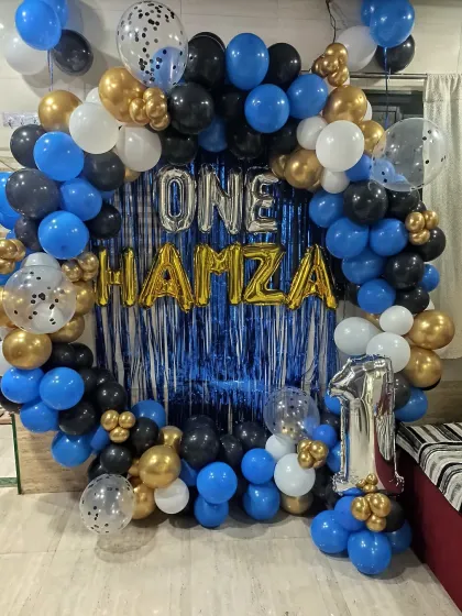 A stylish balloon ring decoration perfect for a home party. This setup for a first birthday uses a blue fringe curtain and a black, blue, and gold balloon arrangement.