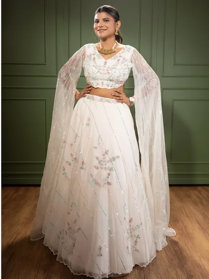 This elegant white lehenga features delicate floral embroidery and dramatic flared sleeves. It’s a timeless piece that is perfect for an engagement party or a sophisticated reception look.