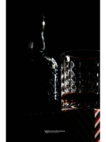 A close-up silhouette of a whiskey glass and bottle. The focus is on the play of light on the crystal, highlighting the premium quality of the glassware and the spirit within.