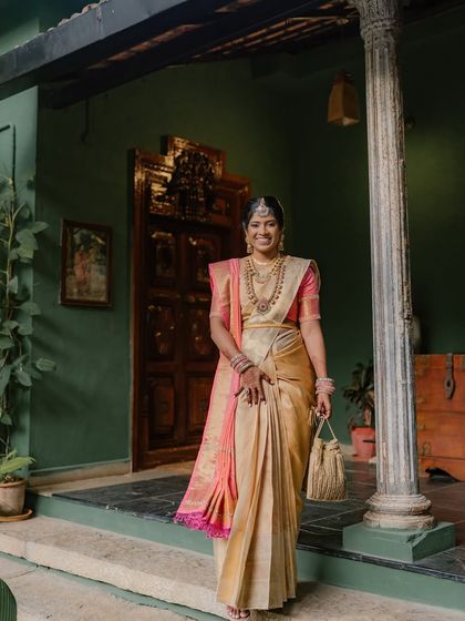 A full-length portrait of a bride in a gorgeous golden saree, standing in the green-walled corridor.