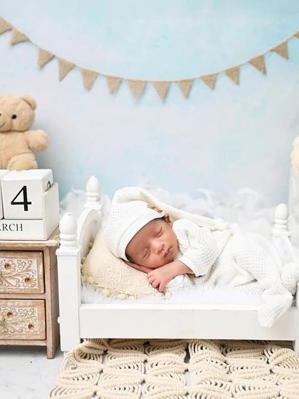 A classic teddy bear theme. This little prince, dressed in a cozy white romper, sleeps soundly in a miniature bed, creating a timeless and adorable portrait.