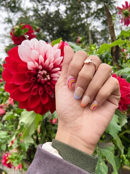 You stole my heart. A beautiful shot of my rainbow-themed nails against a vibrant red flower, capturing the beauty of nature on a trip.