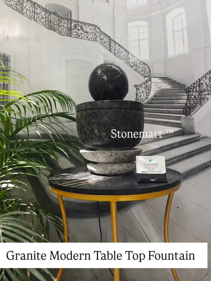 A modern tabletop fountain carved from granite. The piece features a dark granite sphere and bowl, resting on a lighter granite base, creating a beautiful contrast.