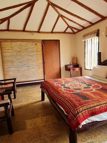 A cozy and rustic room at the Lacuna Eco-stay in Coorg. The design uses natural materials that blend with the surroundings, offering a comfortable and authentic retreat with activities like coffee tours and guided treks available.
