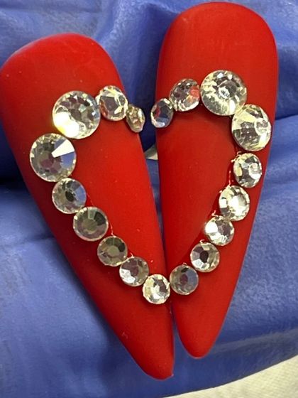 A creative Valentine's concept, with two nails coming together to form a heart made of brilliant rhinestones on a matte red base.