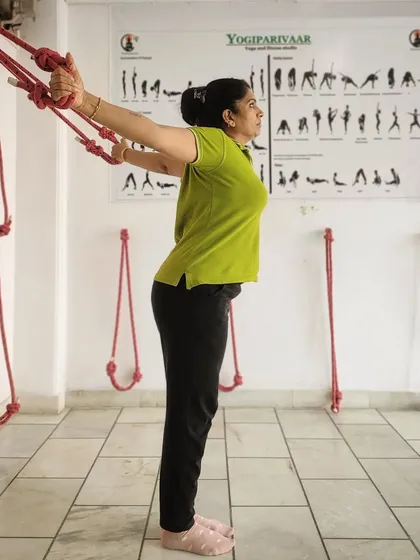 A side view of a student using the wall ropes. This method allows for a deep, supported stretch that helps decompress the spine and improve shoulder mobility, making it accessible even for those with stiffness.