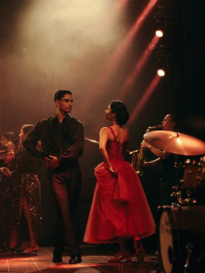 A candid moment between the lead dancers for the Origin & Ode campaign. The styling, with the vibrant red dress and classic menswear, was chosen to evoke a timeless, romantic feel.