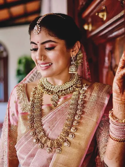 A duplicate of image 125, a smiling bride in her pink Kanchipuram saree, showing a close-up of her custom embroidered blouse.