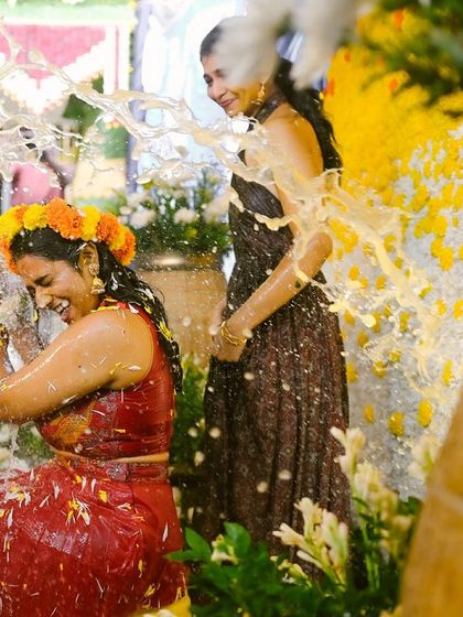 A joyful moment from a Haldi ceremony, with the bride laughing as she is showered with milk and flowers.