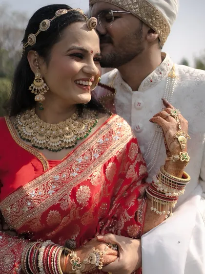 A moment of pure adoration. The groom whispers to his radiant bride, whose smile says it all. Her stunning red Banarasi saree and intricate gold jewelry make this a truly regal portrait.
