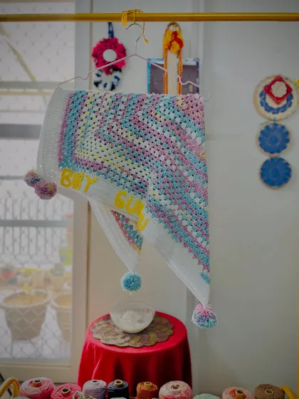 The "Baby Gunnu" blanket displayed on a hanger, giving a sense of its size and drape. It’s a cozy and warm wrap, perfect for a newborn.