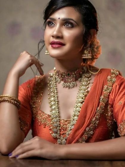 A thoughtful pose showing a bride-to-be in an orange saree, adorned with a delicate choker and haram set.