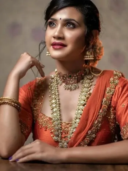An orange silk saree paired with antique-finish jewellery. The makeup is warm and glowing.